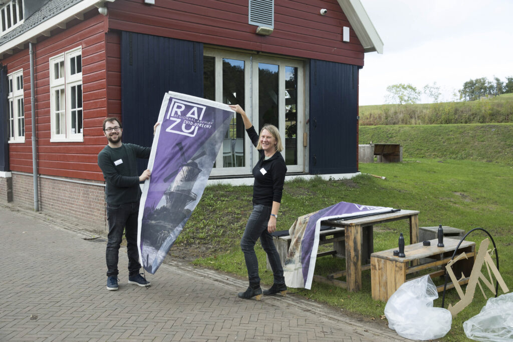 Foto 25 jaar jubileum RAZU op 15 oktober 2021 door Hans Dirksen. Op deze foto poseren Erika Hokke en Steven Brouwer met een RAZU vlag