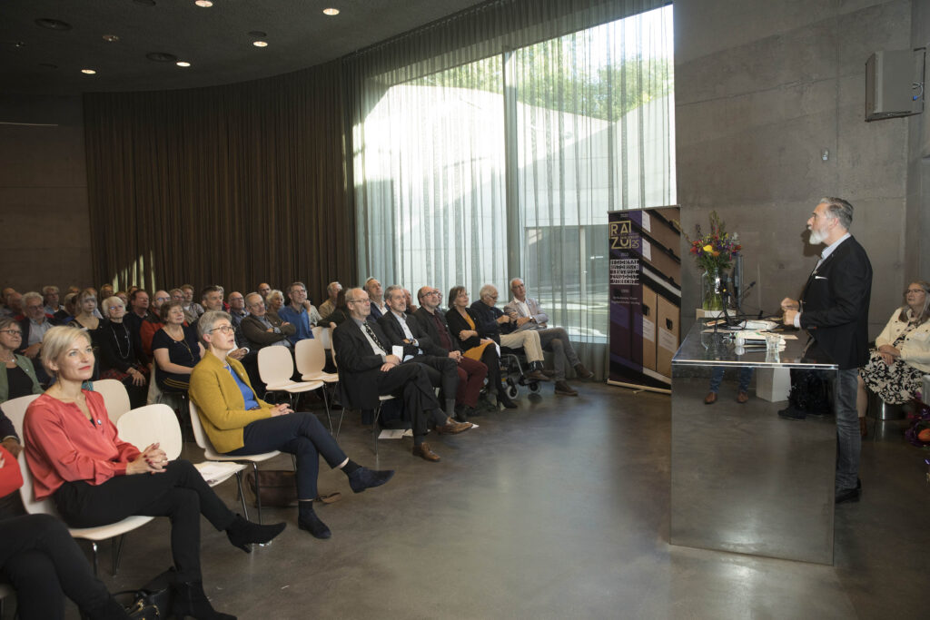 Foto 25 jaar jubileum RAZU op 15 oktober 2021 door Hans Dirksen. Raymond Uppelschoten spreekt de zaal toe en presenteert het liber amicorum ter ere van Ria van der Eerden.