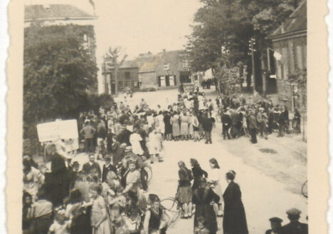 Groep mensen op het Plein naar aanleiding van de bevrijding. Links het gemeentehuis met daarop de Nederlandse vlag, 1945 Houten. Cat.nr. 45795