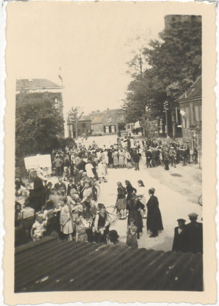 Groep mensen op het Plein naar aanleiding van de bevrijding. Links het gemeentehuis met daarop de Nederlandse vlag, 1945 Houten. Cat.nr. 45795