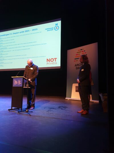 Foto van juryvoorzitter Frits Duparc en Wietse Bakker tijdens het voorlezen van het juryoordeel op de KVAN Archiefdagen 2022 in Alkmaar.